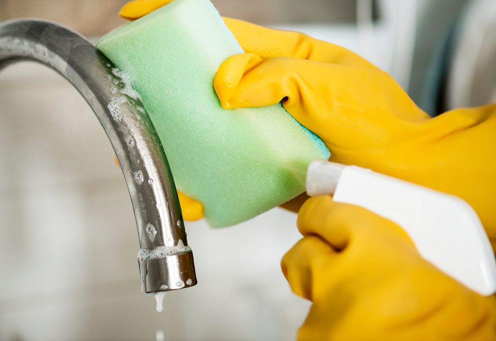 Closeup of hands wearing gloves cleaning the sink faucet domestic chores concept