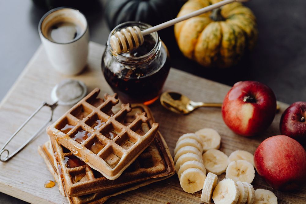 Waffle and slices of banana on a wooden tray next to a honey jar