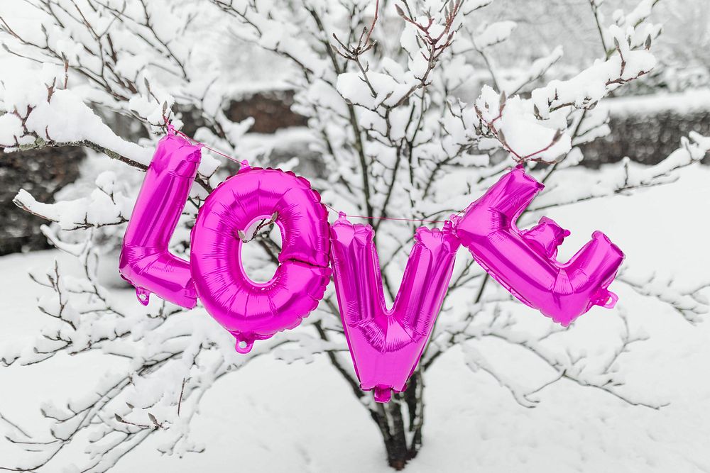 Pink love balloon word hanging on a snowy tree