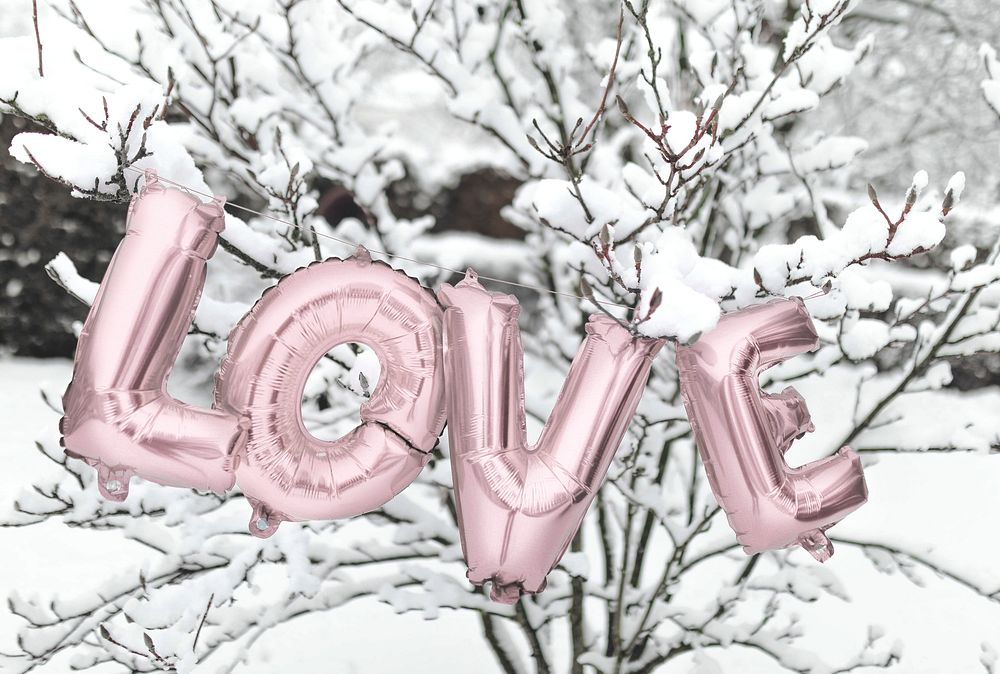 Pink gold love balloon word hanging on a snowy tree