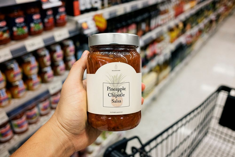 Hand holding a pineapple chipotle salsa in a grocery store