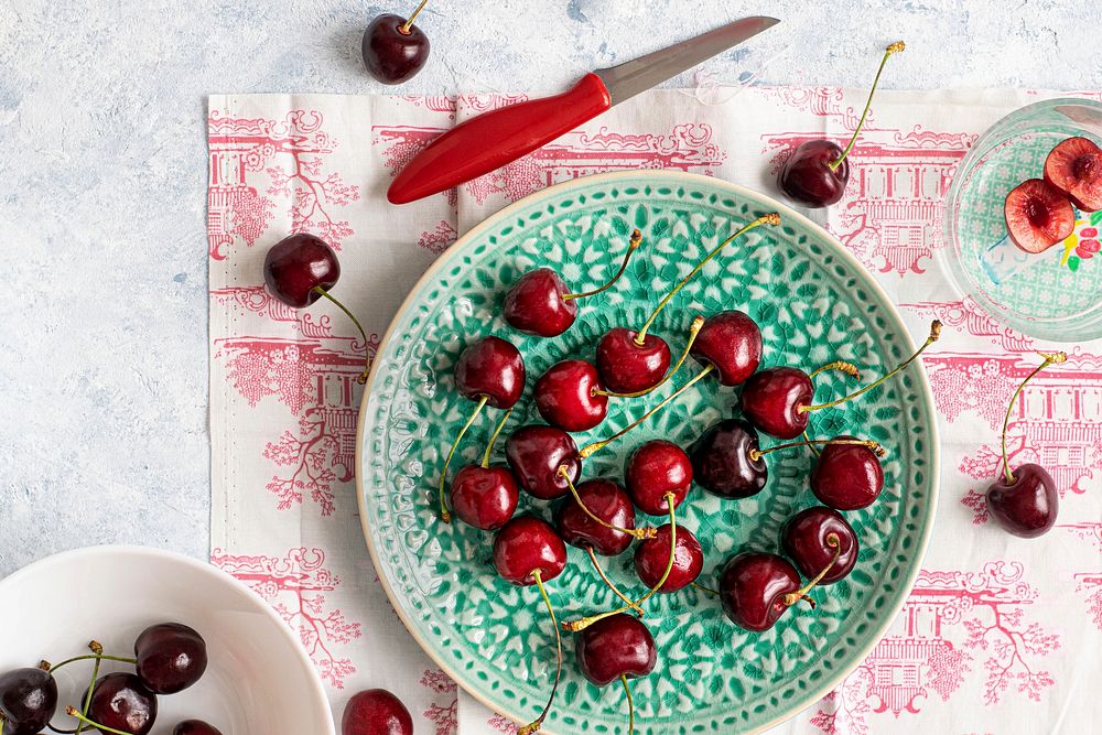 Fresh ripped red cherries on a green plate flatlay