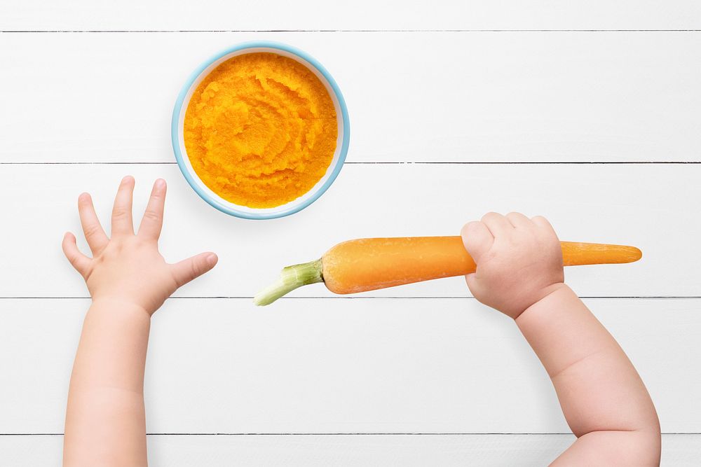 Baby hands psd holding carrot on orange background