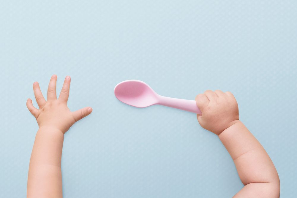 Baby hands psd holding spoon on blue background