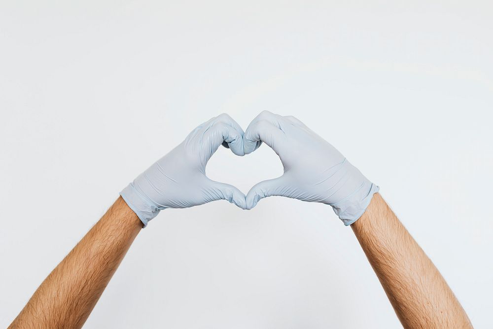 Gloved hands making a heart shaped sign on a gray background