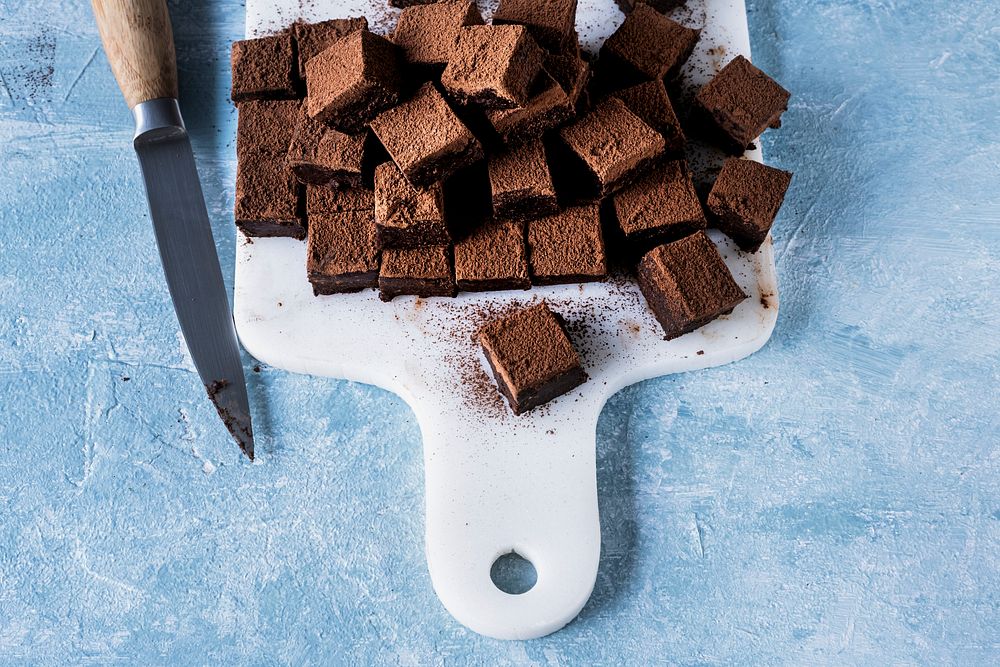 Chocolate ganache truffle squares dusted with cacao being cut into cubes 