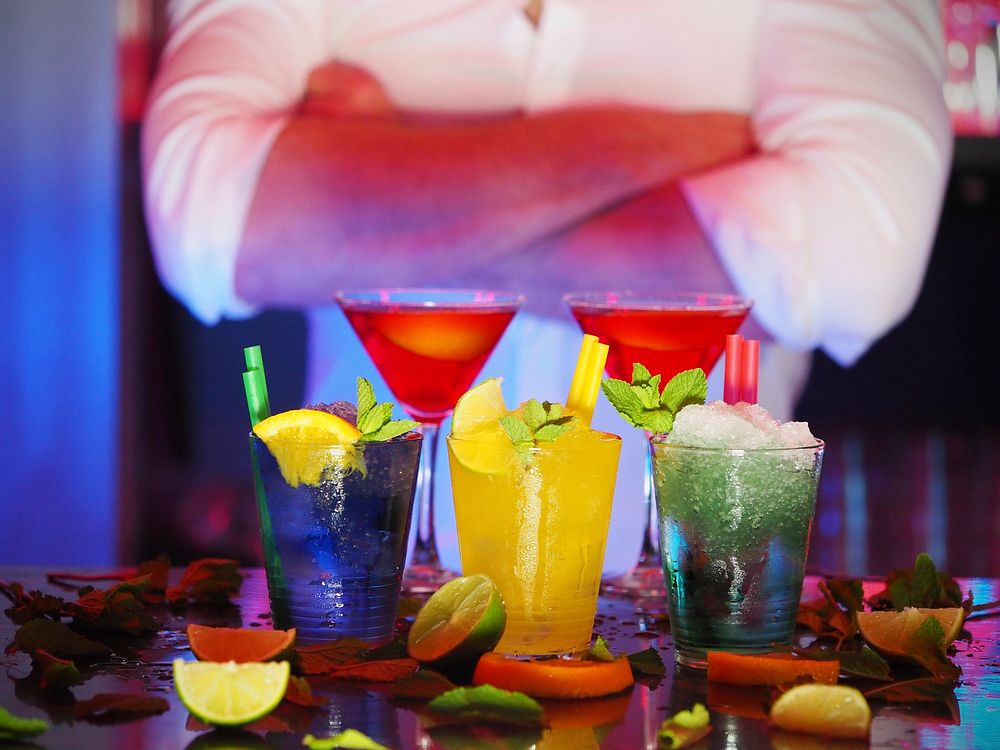 Free cocktail glass on bar counter with bartender in background photo, public domain beverage CC0 image.