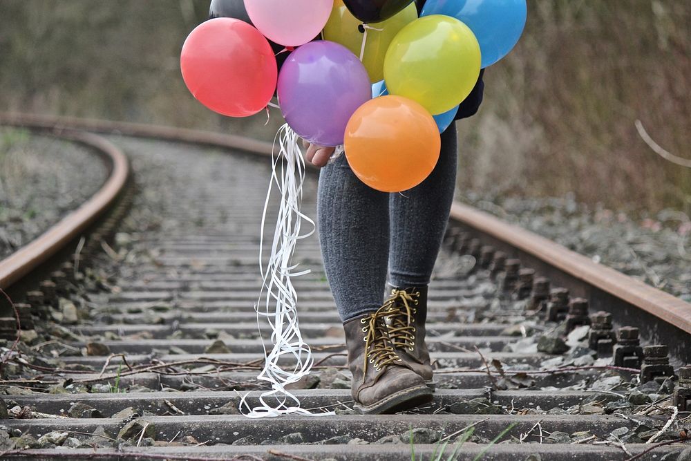 Woman holding balloons, train track image, public domain CC0 photo.