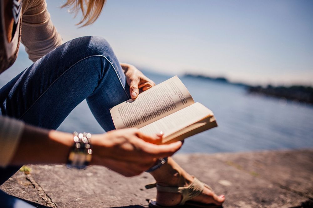 Free person reading a book on beach rock photo, public domain book CC0 image.