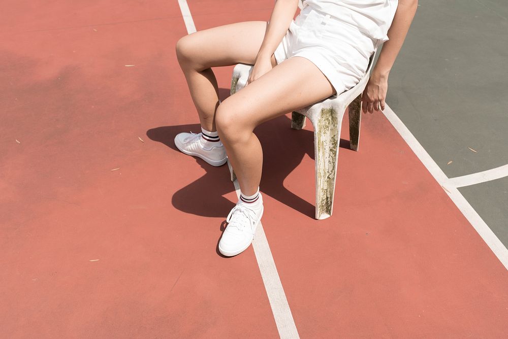 Free person wearing white shorts sitting on plastic chair beside green court image, public domain sport CC0 photo.