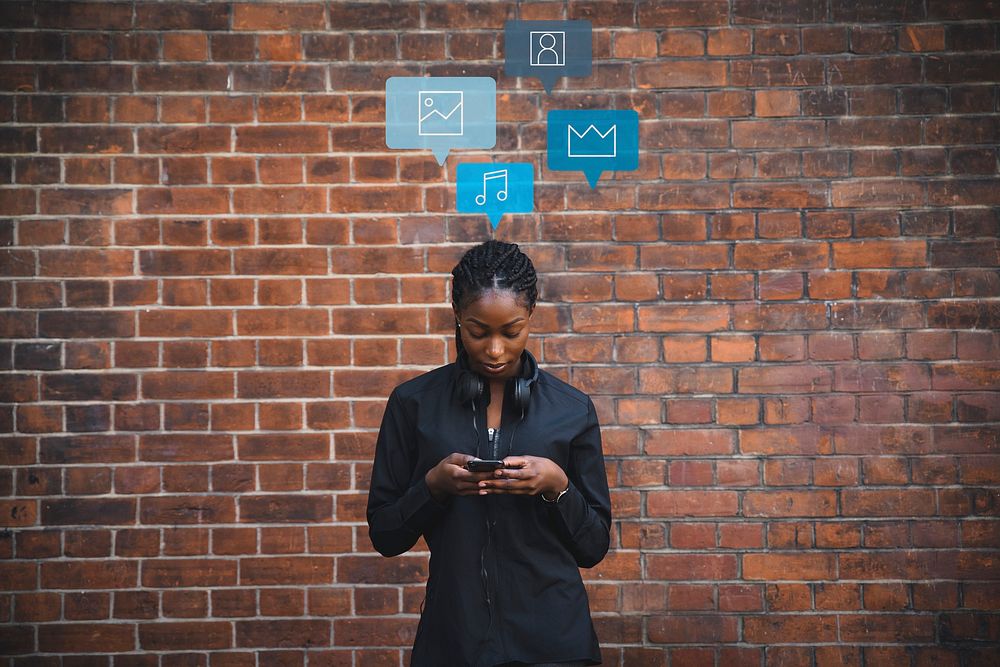 Black woman using her phone in front of a brick wall
