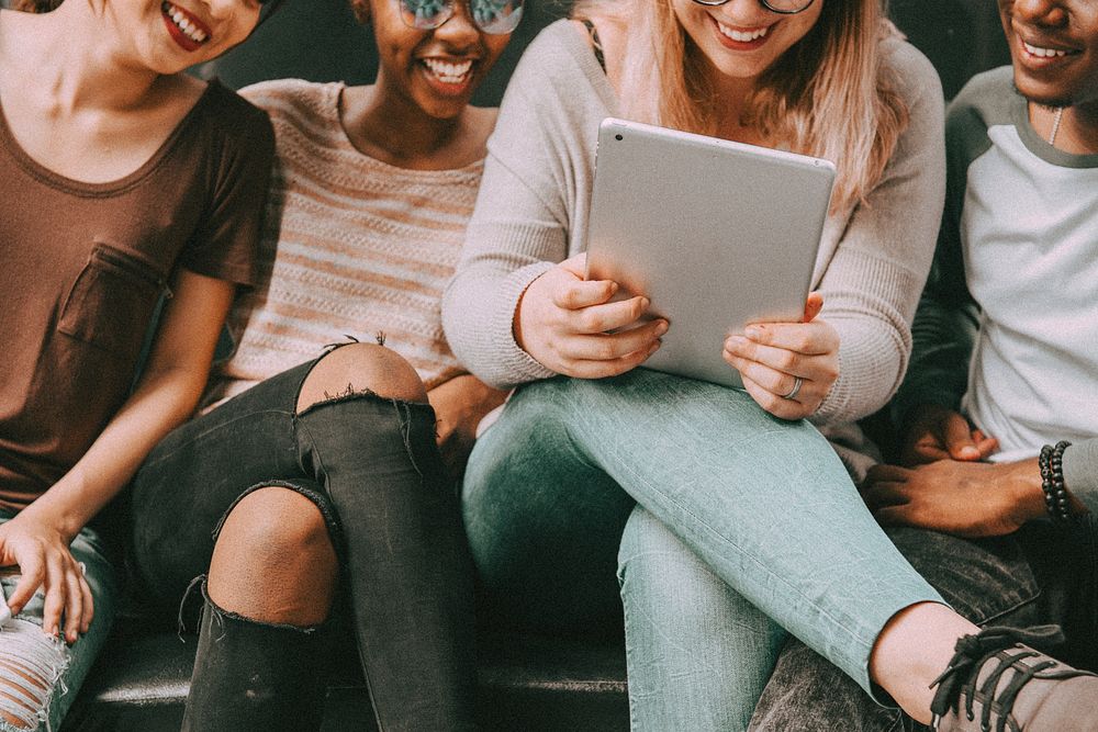 Friends laughing, holding a tablet while hanging out together
