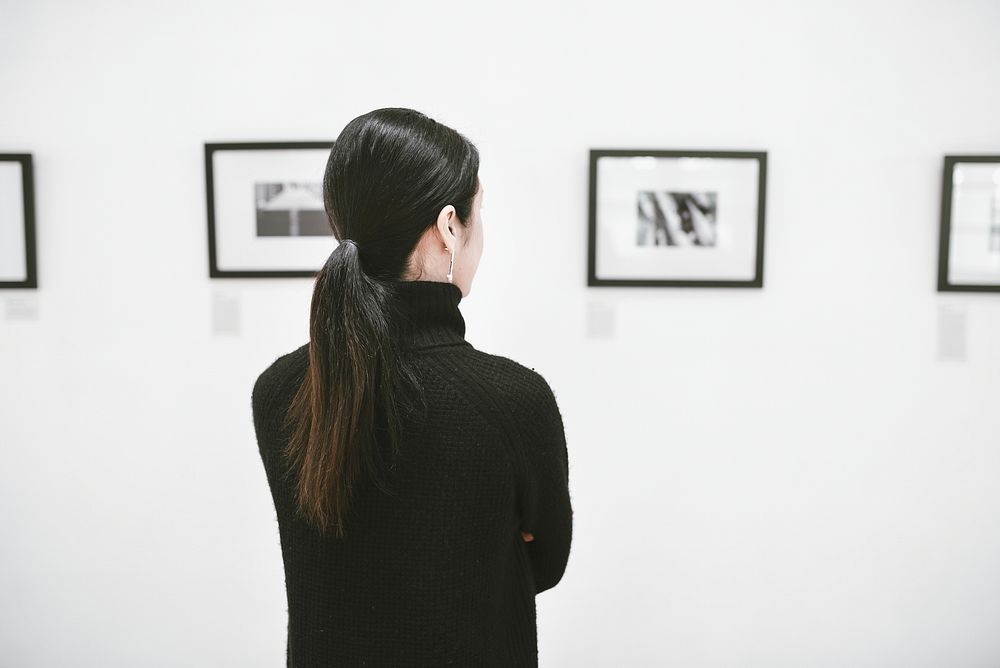 Woman admiring paintings in art gallery rear view photo