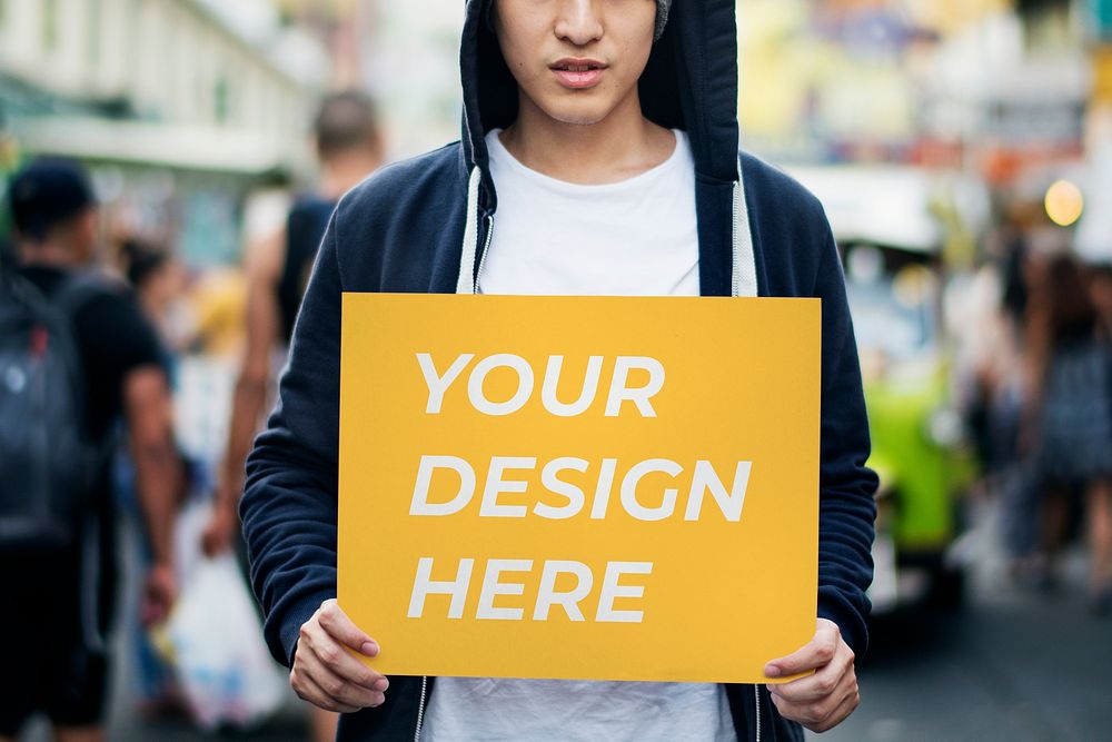 Young Asian man holding a placard mockup outdoors