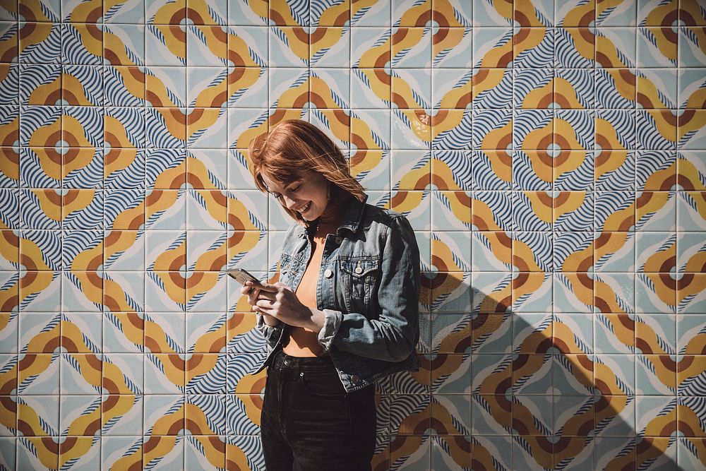 Woman using phone by modern patterned wall