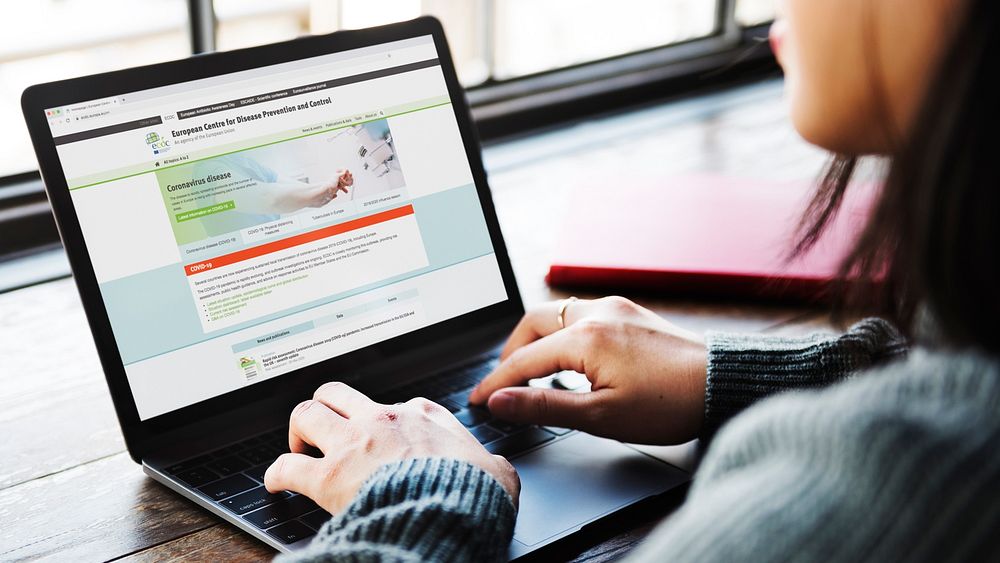 Woman reading coronavirus information from a laptop mockup with editorial graphic from https://www.ecdc.europa.eu/en…