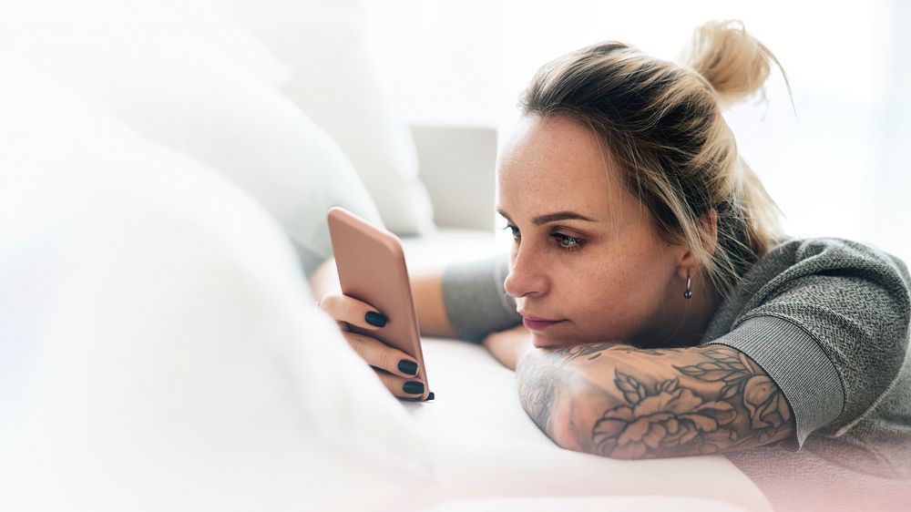 Tattooed woman texting on a couch
