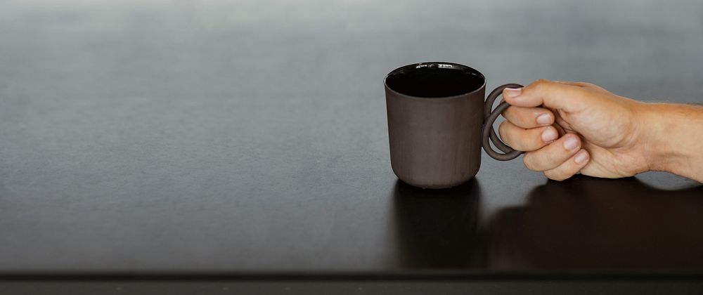 Hand holding a black coffee cup on a black table