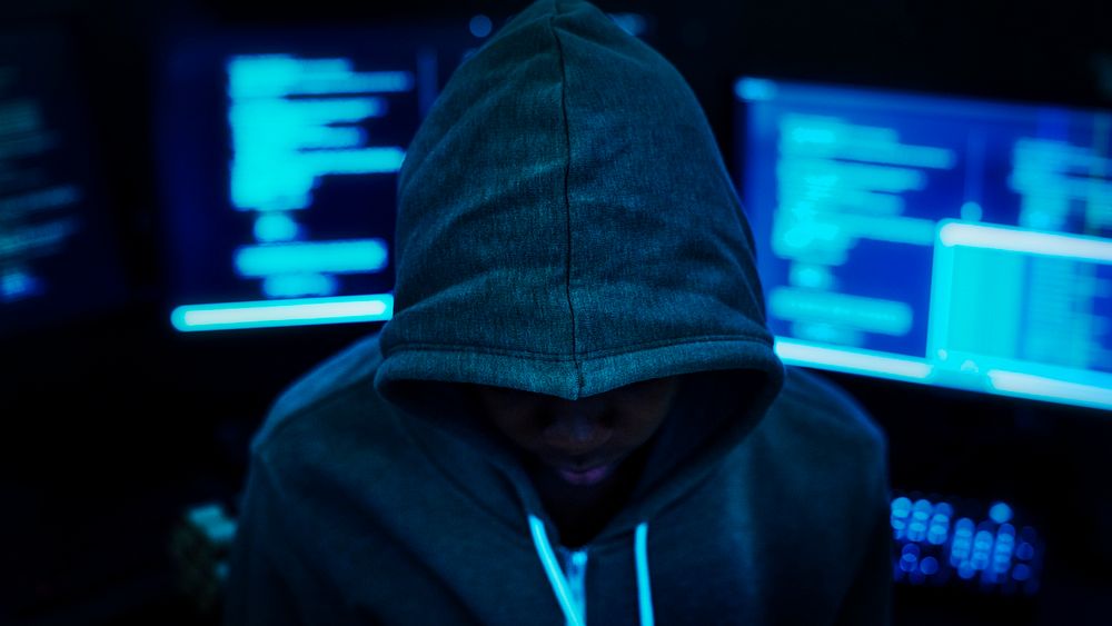 Hacker wearing a hoodie with computers in the background