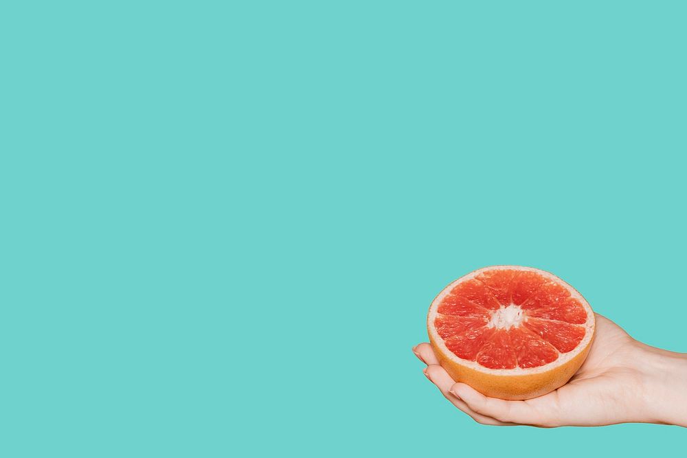 Hand holding a fresh grapefruit on a green background