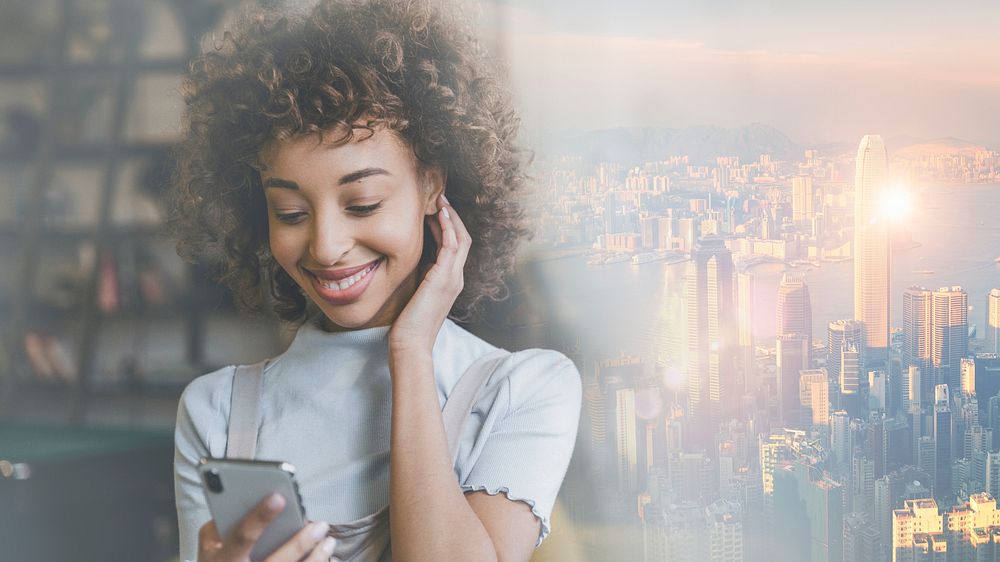 Woman connecting on social media smiling at her phone over city background