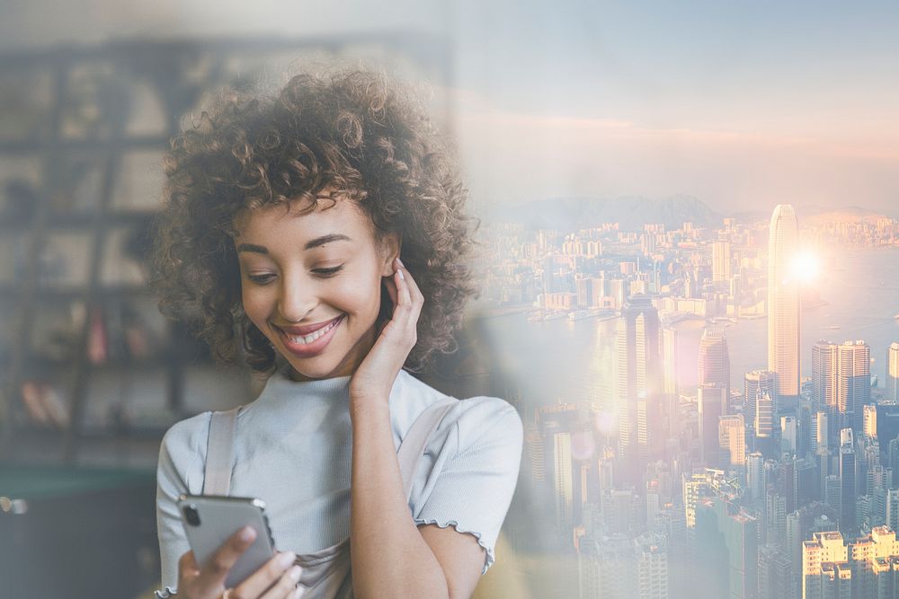 Woman connecting on social media smiling at her phone over city background