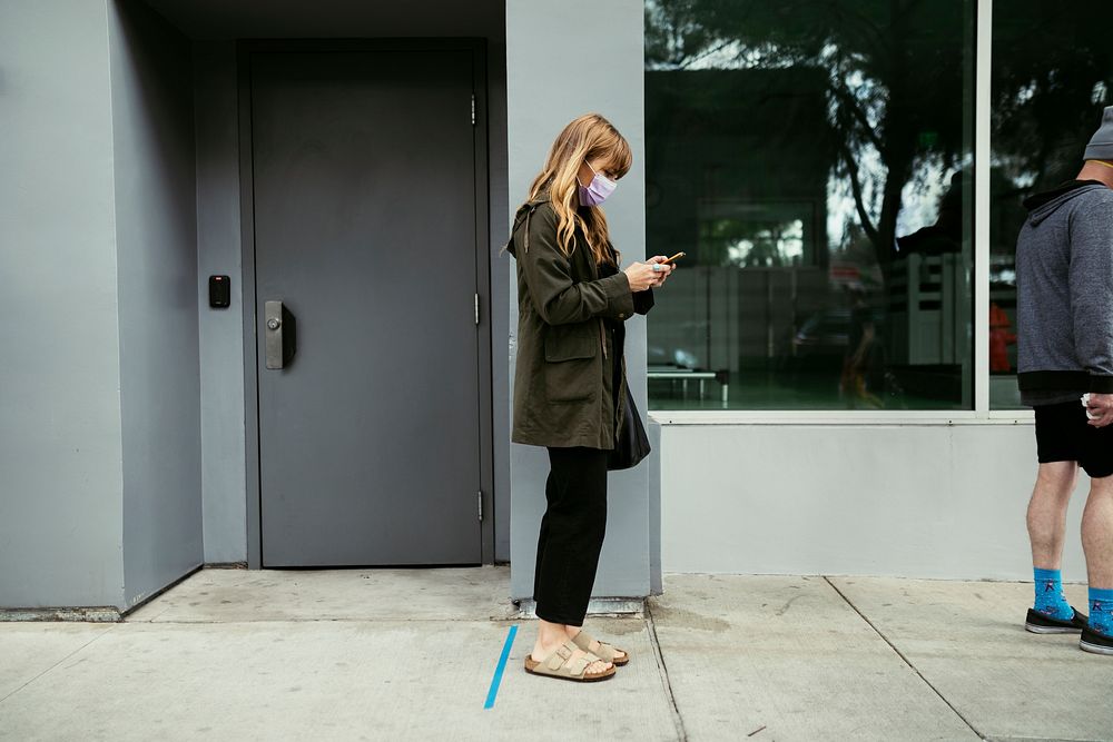 People using their phones and having social distancing while line up during coronavirus pandemic