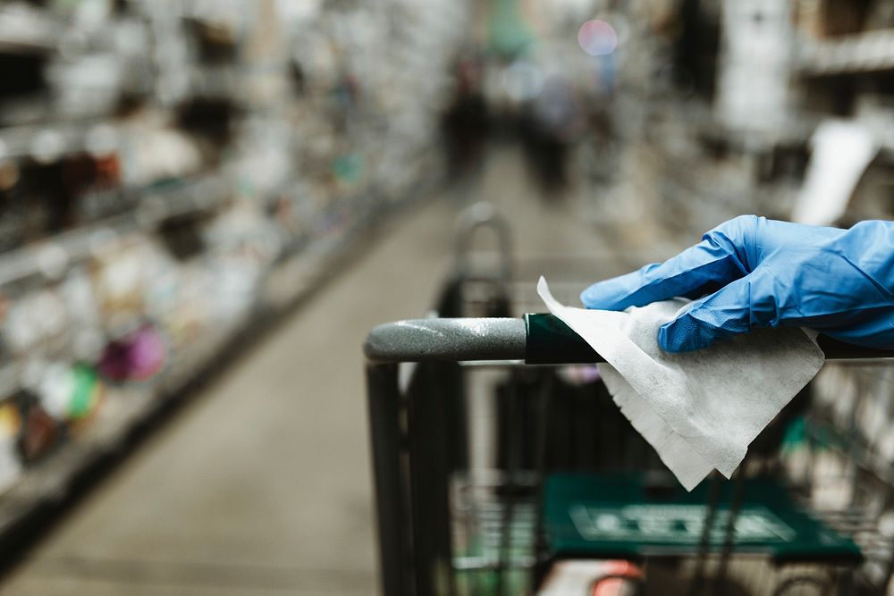 Gloved hand with a tissue paper on a shopping cart in a supermarket during the Coronavirus pandemic
