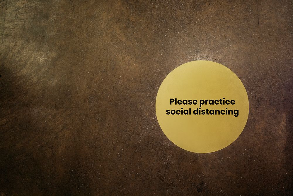 Please practice social distancing yellow sign on a brown background
