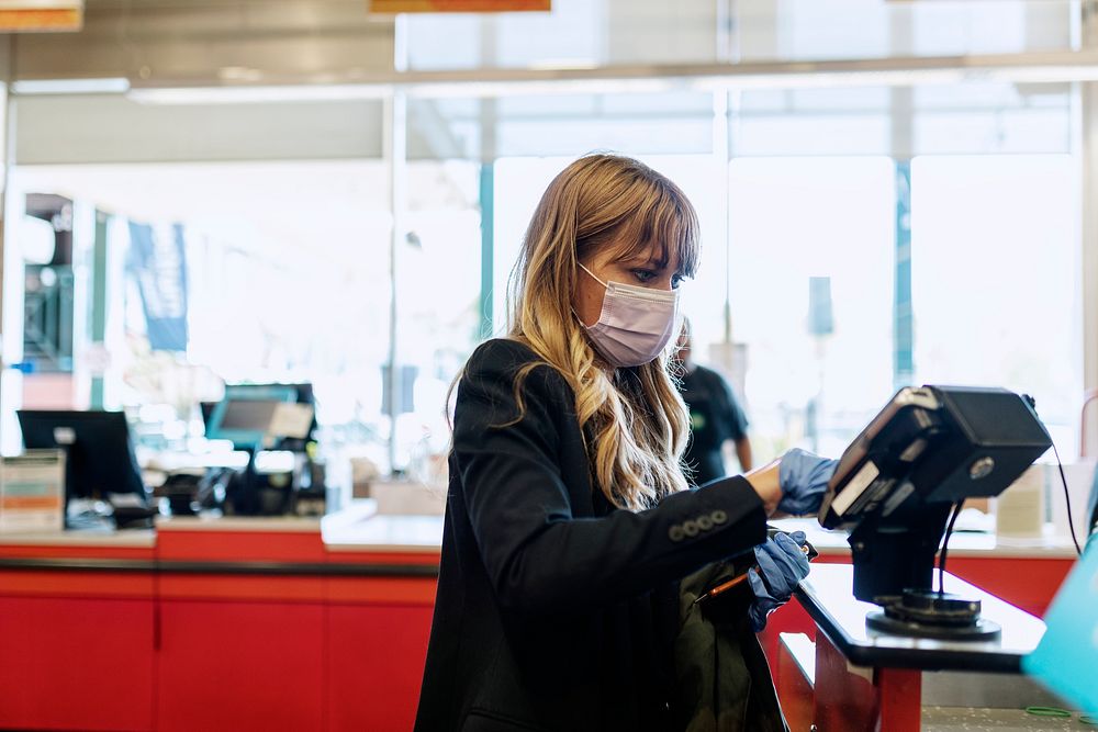 Woman in a face mask wearing latex gloves while purchasing at a self-checkout in a supermarket during coronavirus quarantine