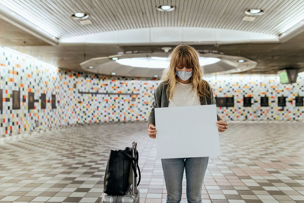 Woman with a suitcase holding a blank paper during the coronavirus outbreak