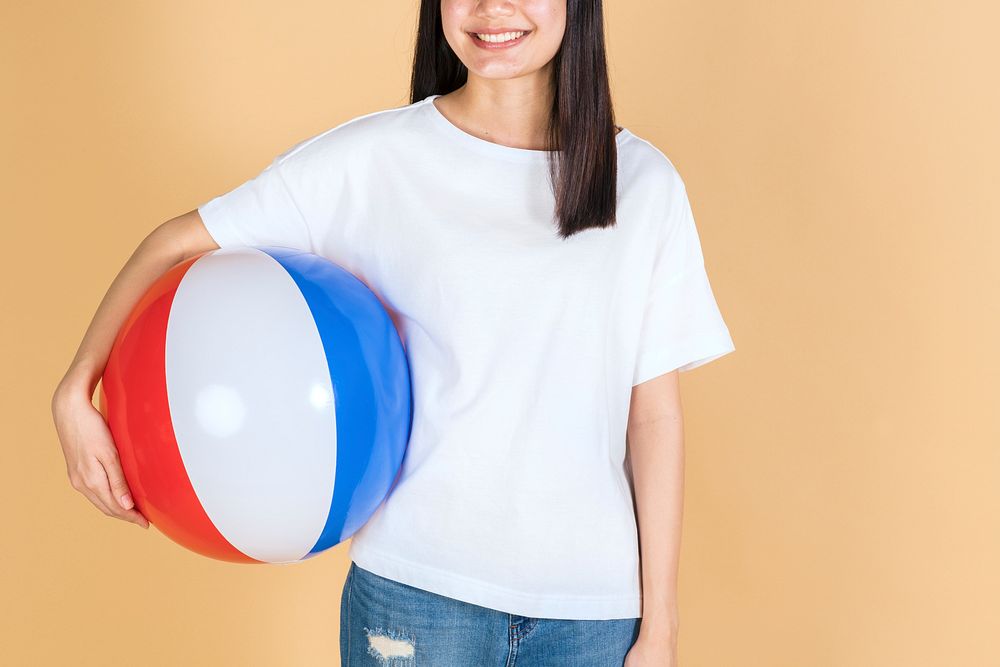 Woman in a white tee mockup holding a beach ball on a beige background