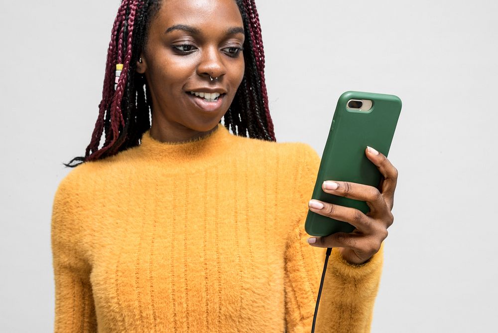 Cheerful black woman using a cellphone while it charging