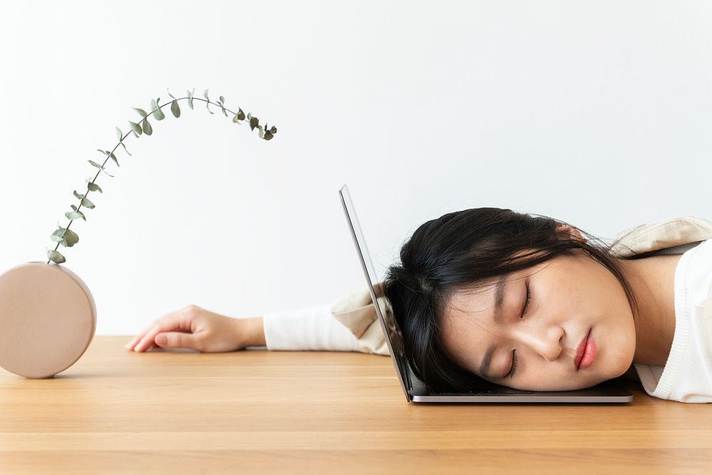 Tired Asian woman resting her head on a laptop 