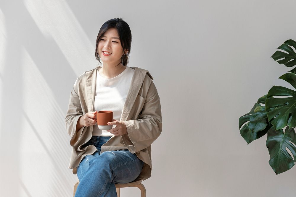 Happy Asian woman sitting on a wooden stool drinking coffee 