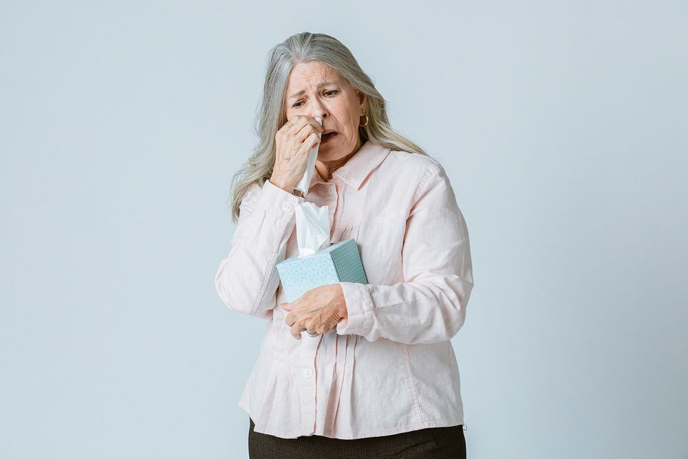 Coronavirus infected senior woman blowing nose into a tissue paper