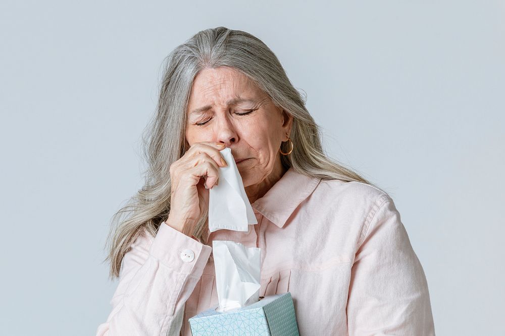 Coronavirus infected senior woman blowing nose into a tissue paper