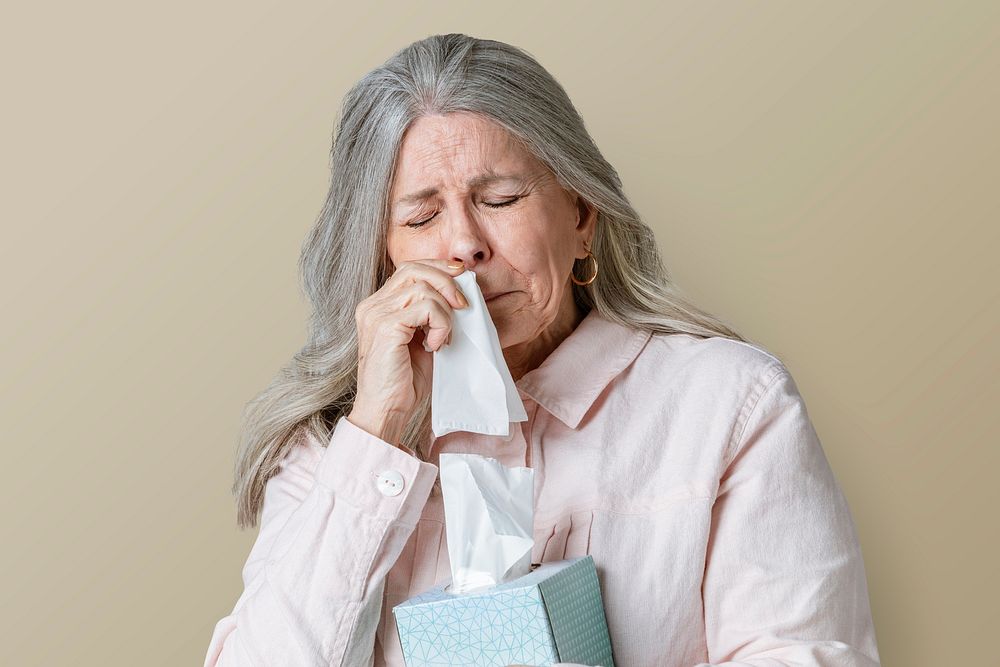 Coronavirus infected senior woman blowing nose into a tissue paper mockup