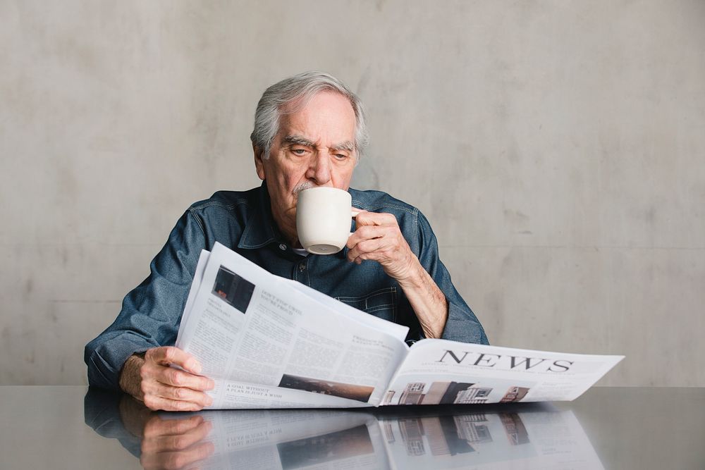 Senior man reading COVID-19 news update and drinking coffee during coronavirus pandemic