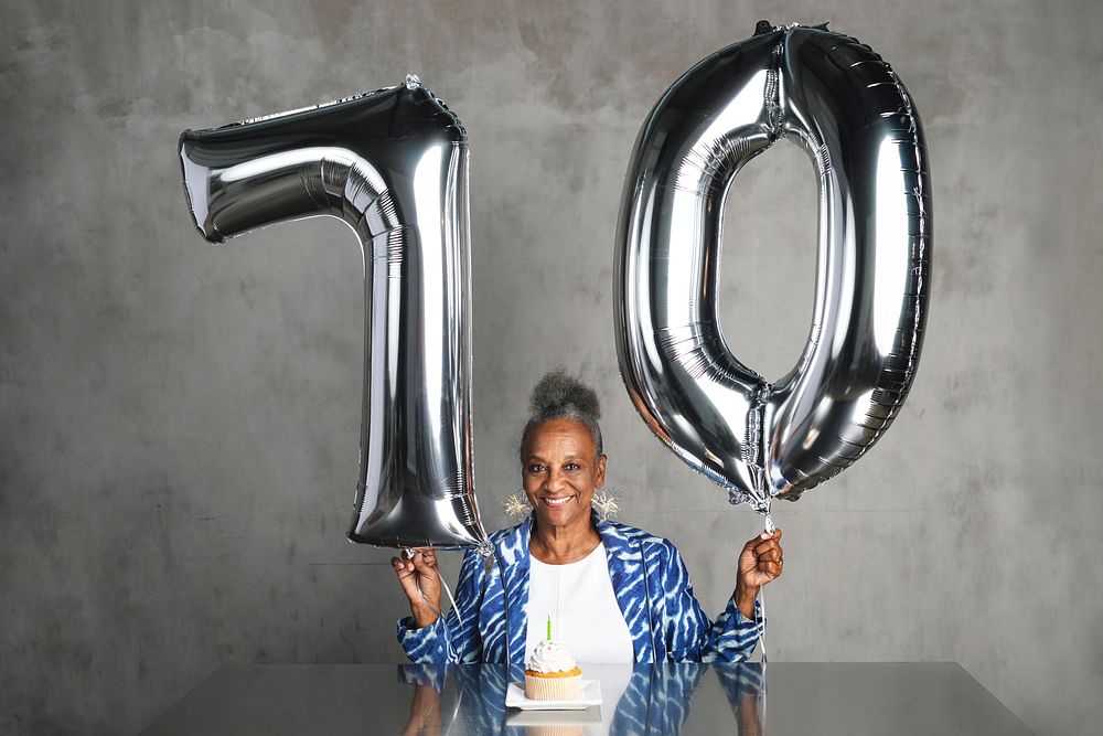 Cheerful senior woman holding silver balloons for her 70th birthday celebration