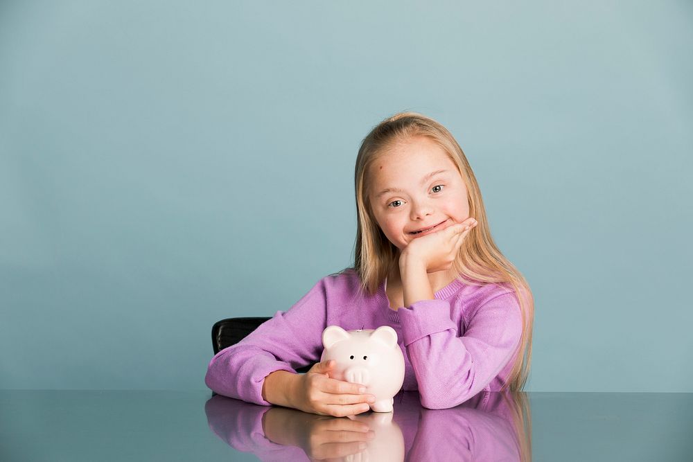 Cute little girl with Down Syndrome saving money in a piggy bank