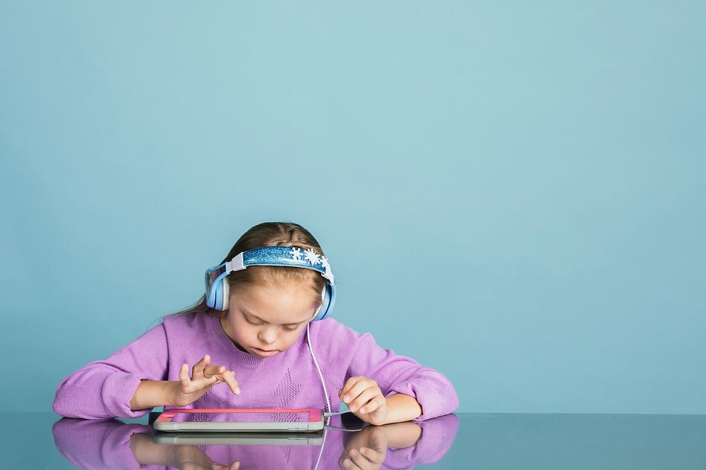 Cute little girl with Down Syndrome playing an online game on a digital tablet