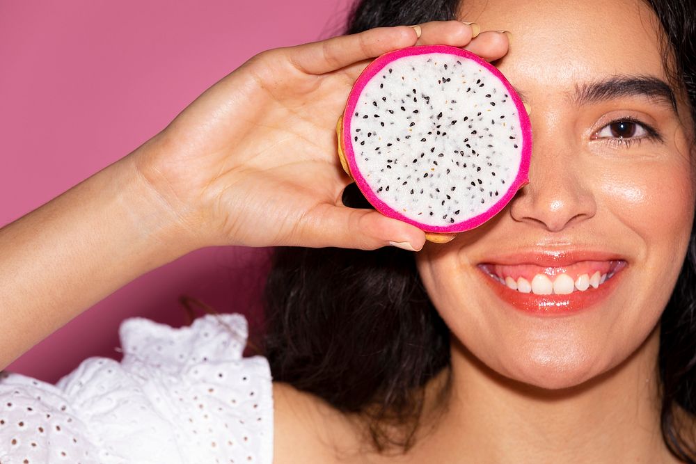 Woman covering her eyes with a sliced dragon fruit