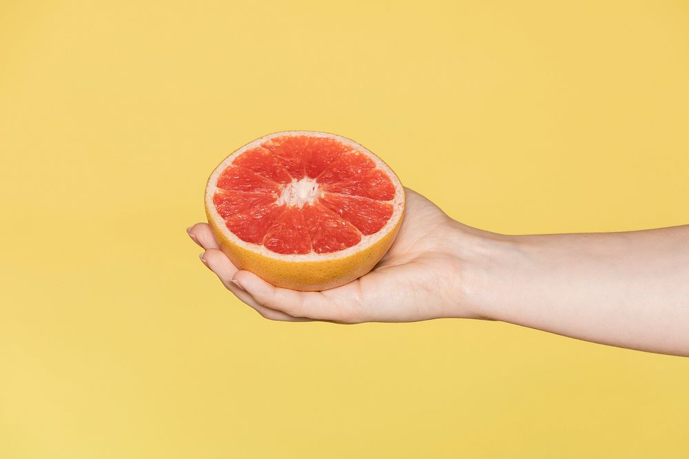 Woman holding grapefruit against a yellow background