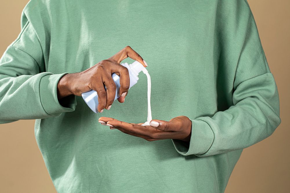 Black woman pumping a white facial cream bottle