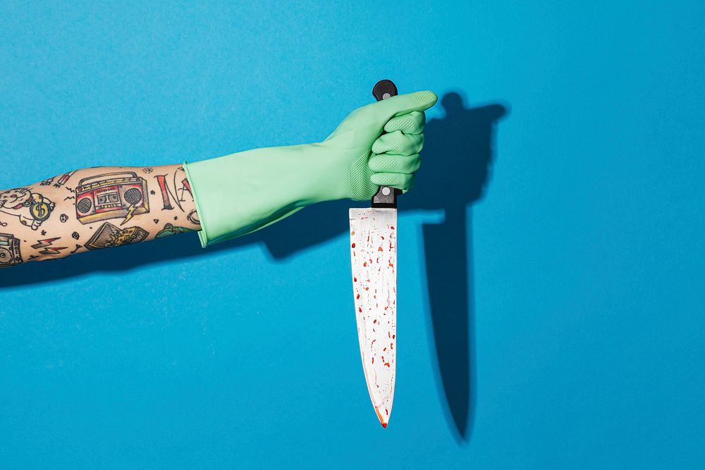 Tattooed feminine hand in a glove holding a knife