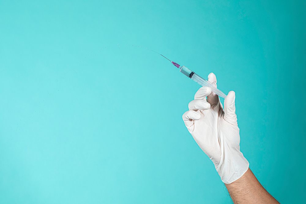 Hand wearing a white glove holding a syringe