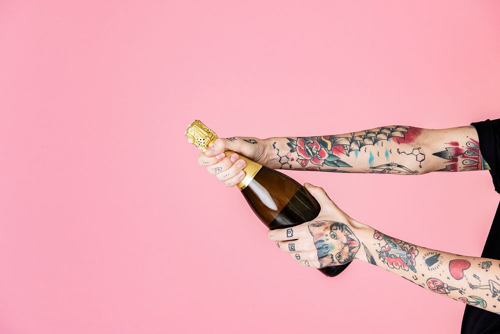 Tattooed feminine hand holding a bottle of champagne