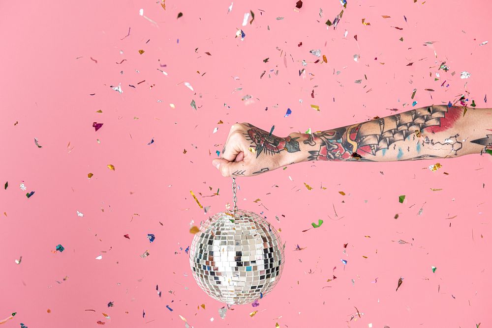 Tattooed hand holding a Christmas disco ball and confetti in the air