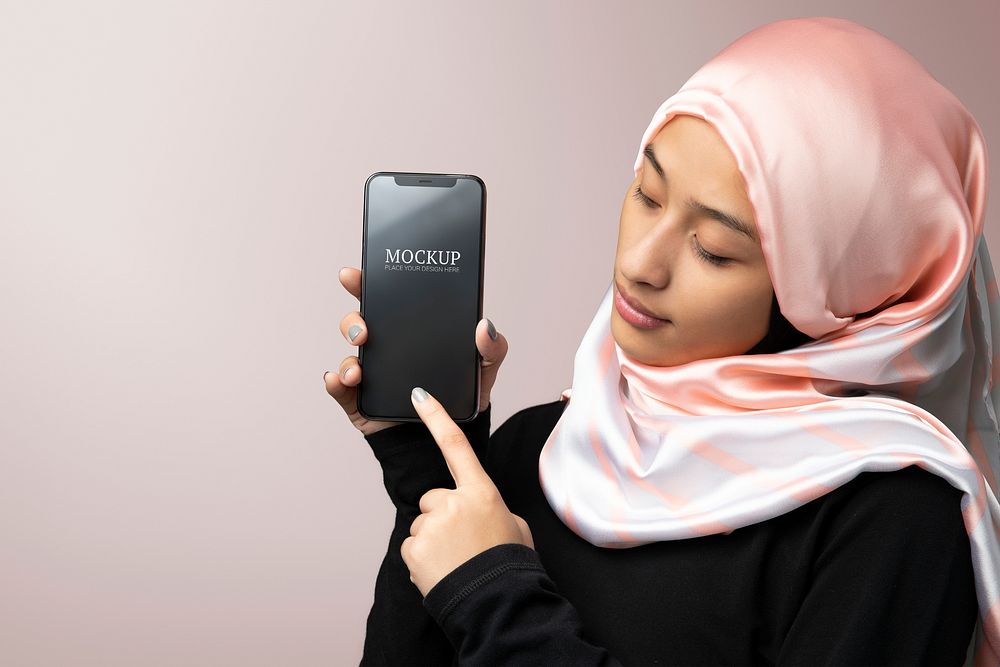 Muslim woman showing a mobile screen mockup in a pink background